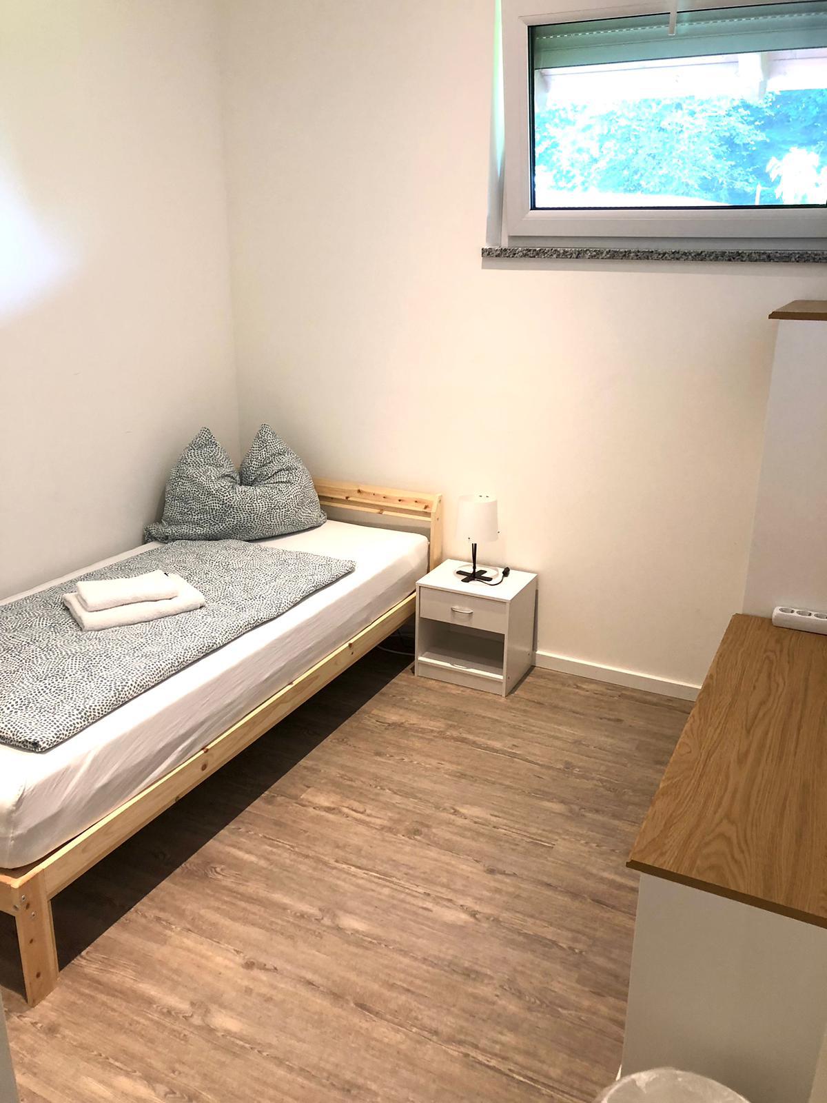 Helles Einzelzimmer mit Bett, Nachttisch und Schreibtisch – Vilstal Apartment 2 in Reisbach/Altersberg