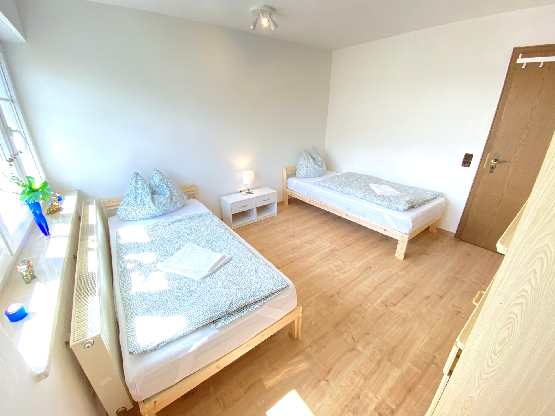 Apartment IV in Kronwieden – Helles Zimmer mit zwei Einzelbetten und Nachttisch am Fenster