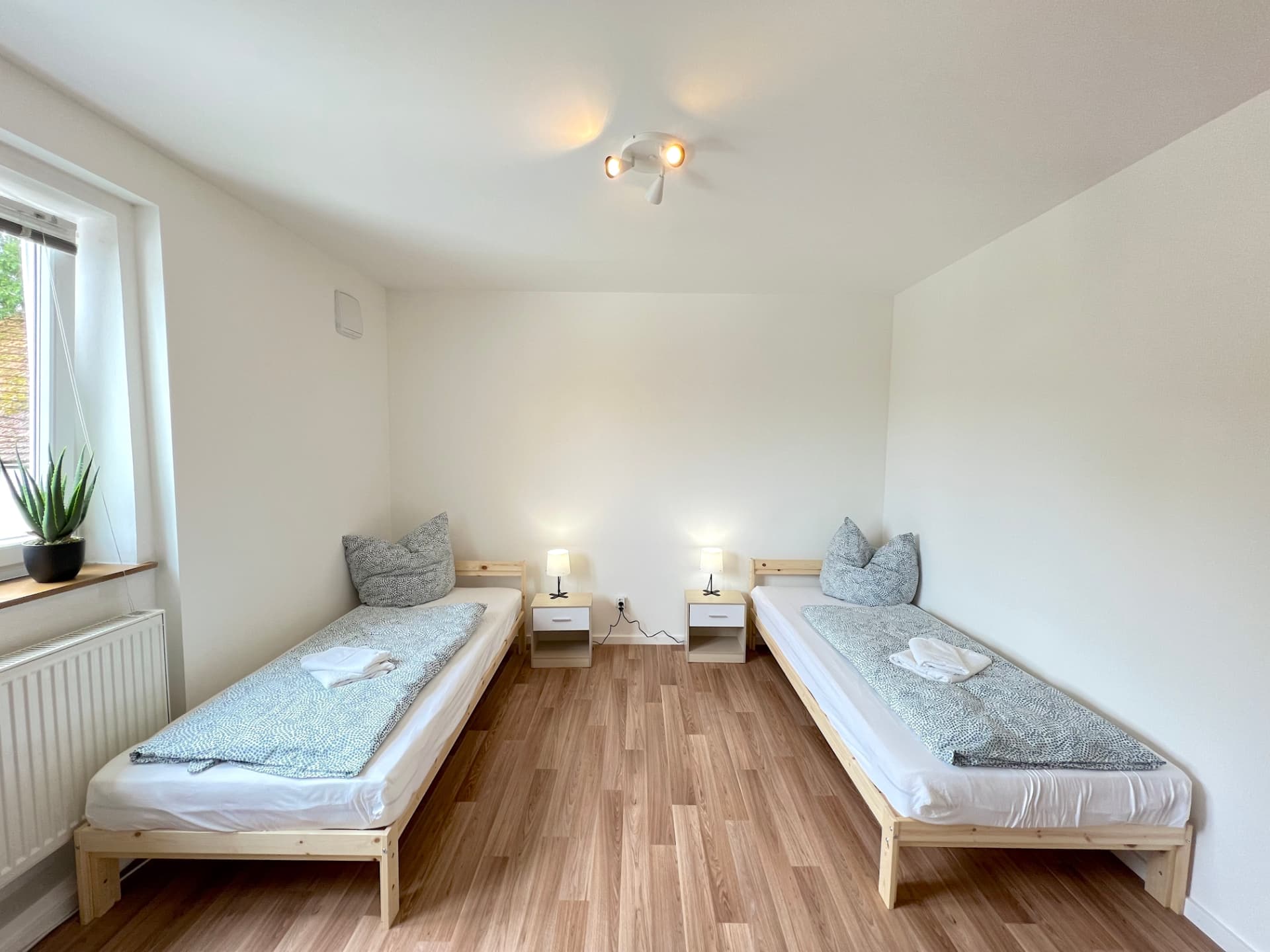 Helles Zwei-Bett-Zimmer mit Holzbetten, Nachttischen und Laminatboden in Apartment I Großköllnbach