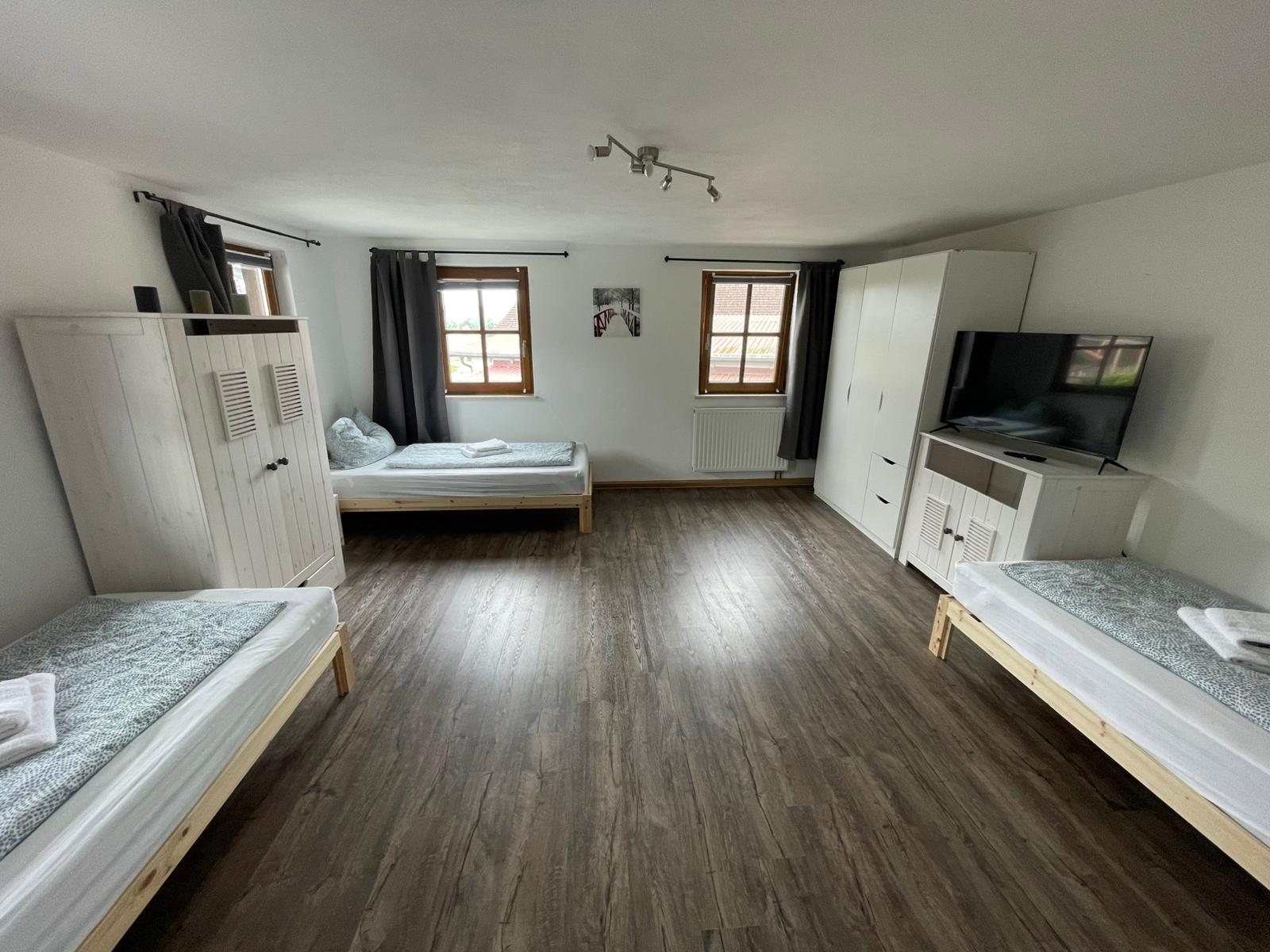 Großer Schlafraum mit drei Einzelbetten, Kleiderschränken und TV – Vilstal Apartment 1 in Reisbach/Altersberg