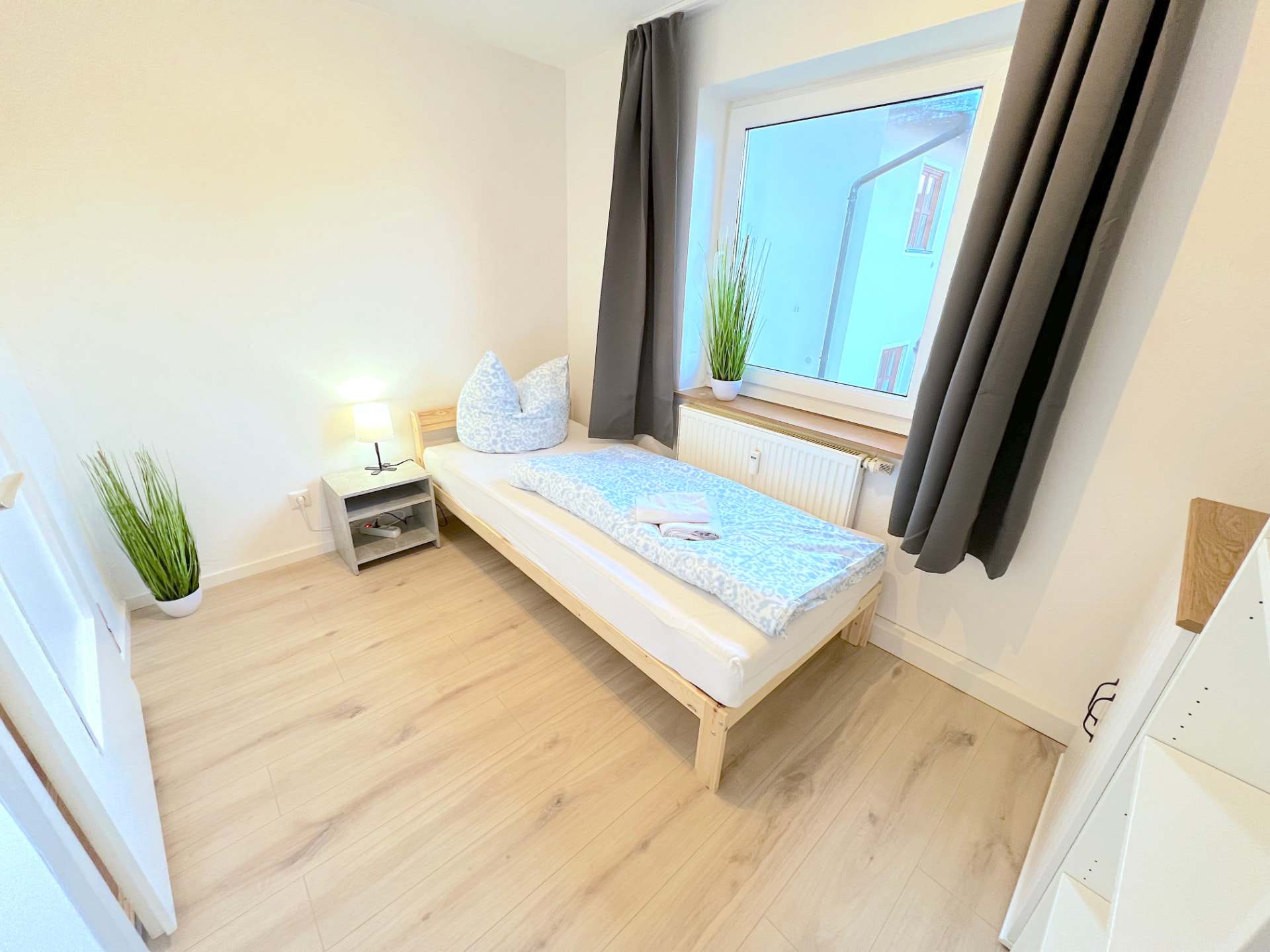 Einzelzimmer mit Holzbett, Nachttisch und großem Fenster in Apartment III Großköllnbach