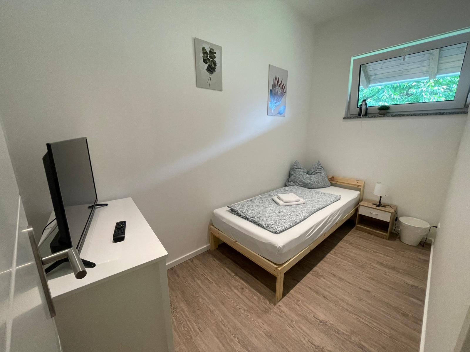 Einzelzimmer mit Holzbett, Nachttisch und TV – Vilstal Apartment 3 in Reisbach/Altersberg