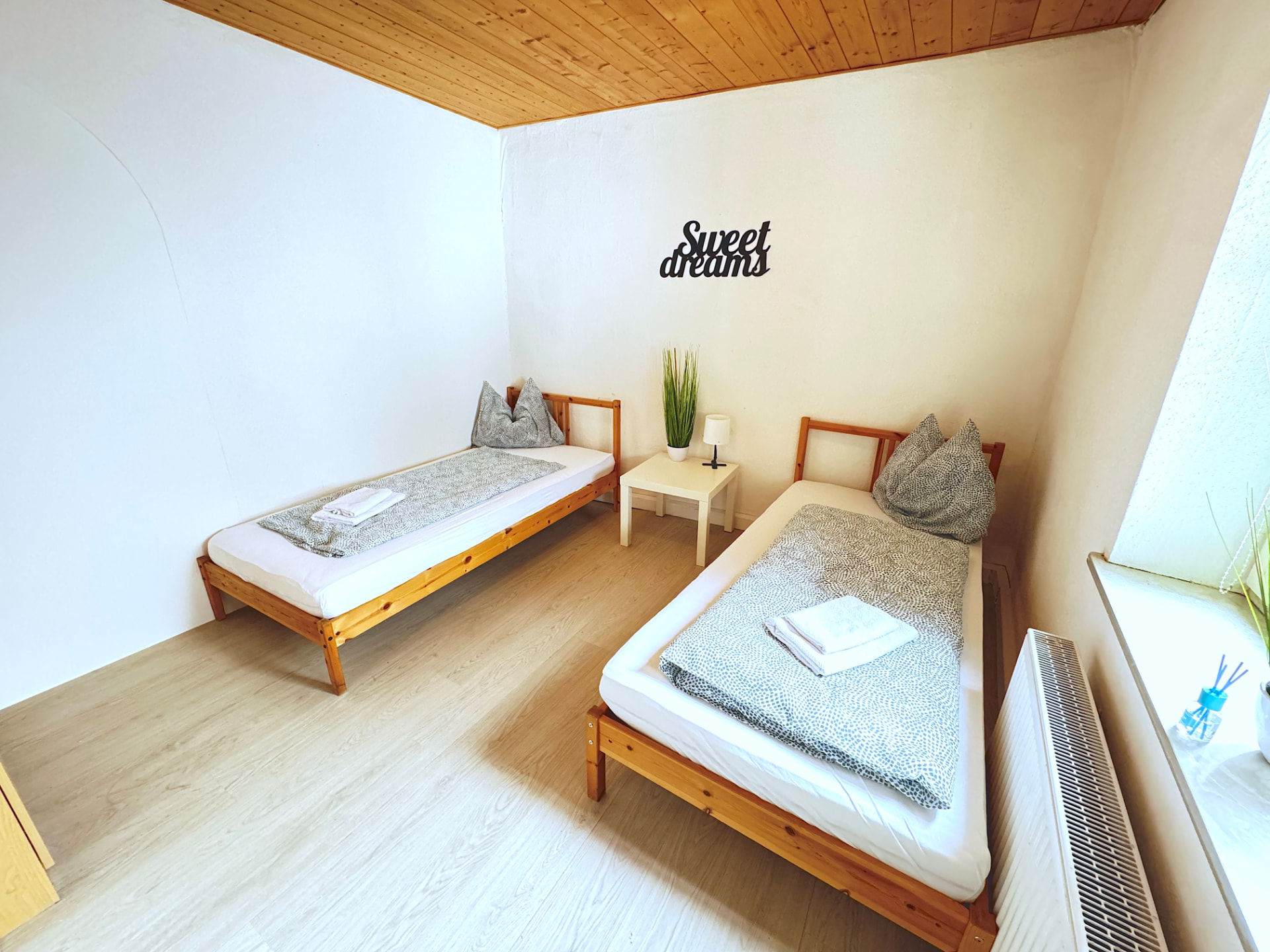 Helles Schlafzimmer mit zwei Einzelbetten, Holzdecke und Sweet-dreams-Schriftzug im Apartmenthaus Großköllnbach