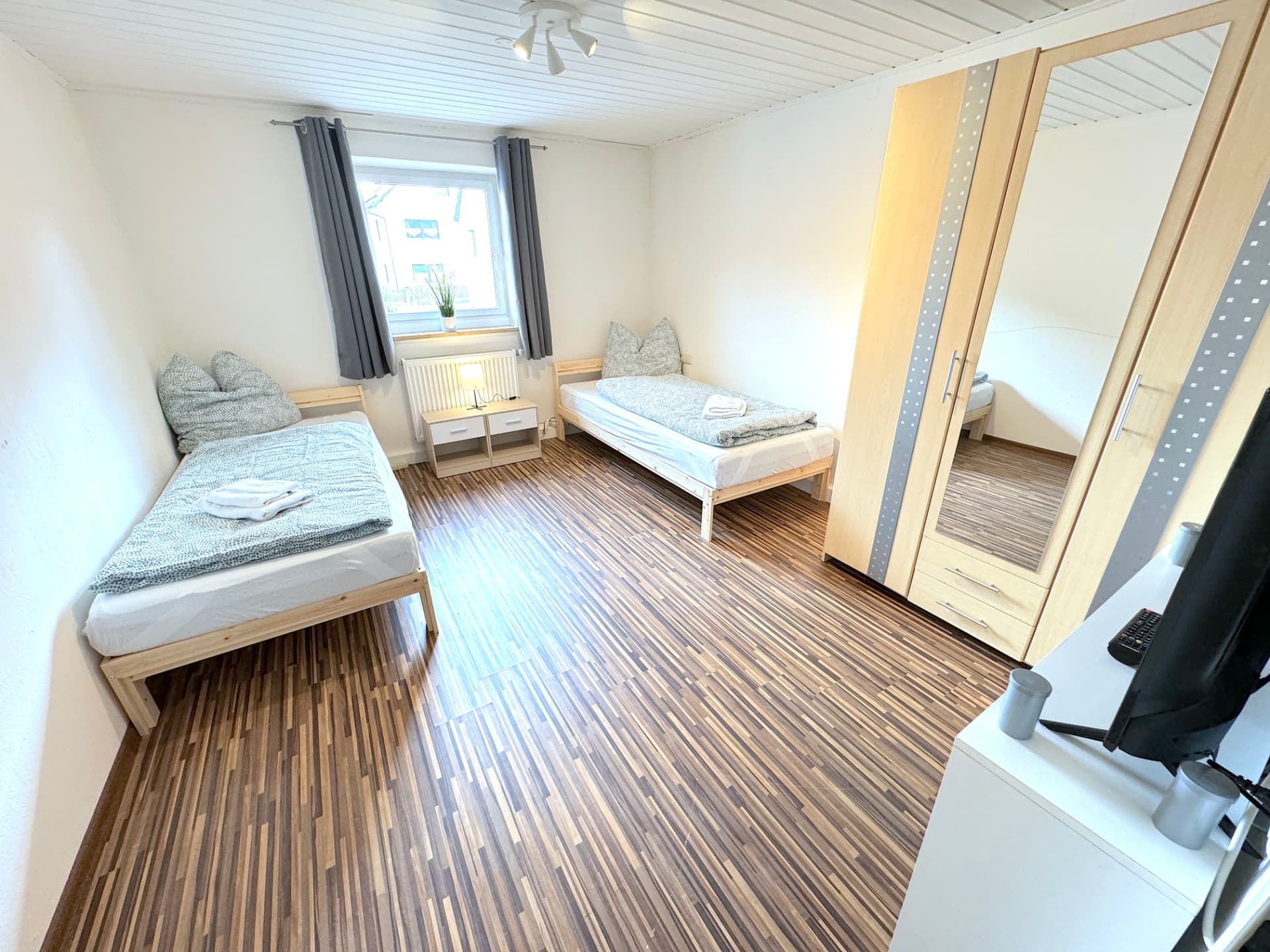 Apartmenthaus in Frontenhausen – Schlafzimmer mit zwei Einzelbetten, Nachttisch und Spiegelschrank