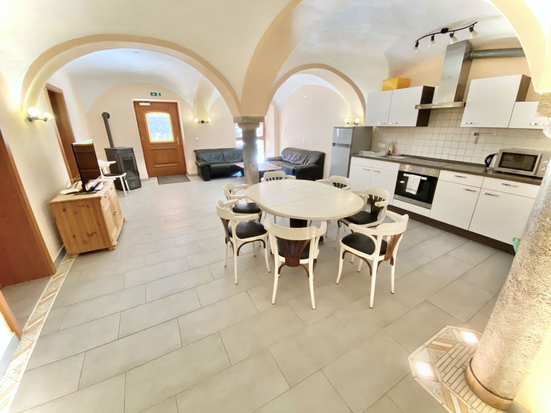 Wohn- und Essbereich mit Gewölbedecke, offener Küche, Esstisch und Ledersofas in Apartment 0 Gottfrieding