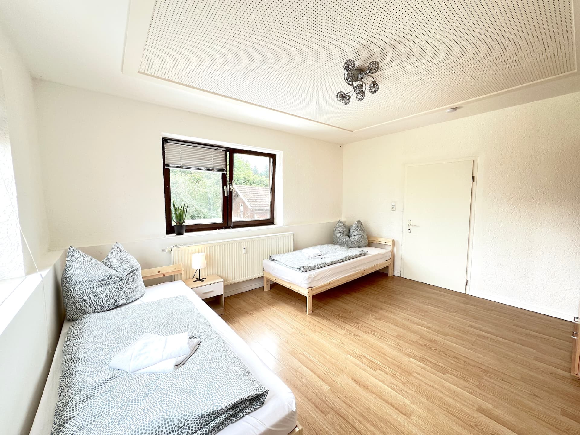 Zwei-Bett-Zimmer mit Fenster, Nachttisch und Holzboden in Apartment I Großköllnbach