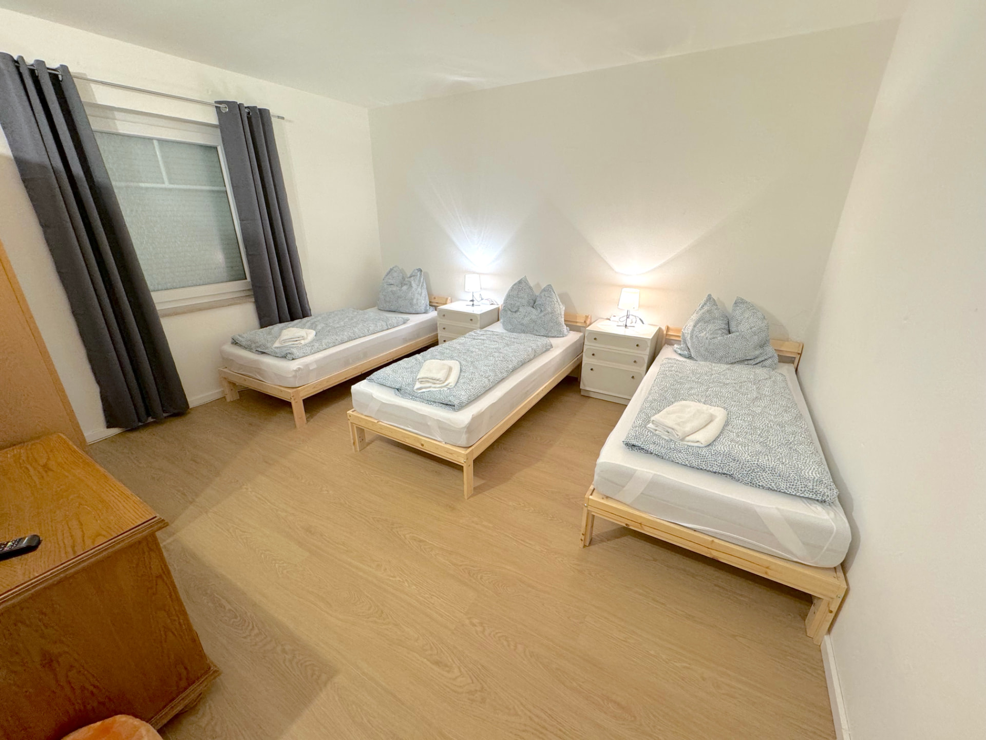 Apartment II in Kronwieden – Zimmer mit drei Einzelbetten, Nachttischen und dunklen Vorhängen
