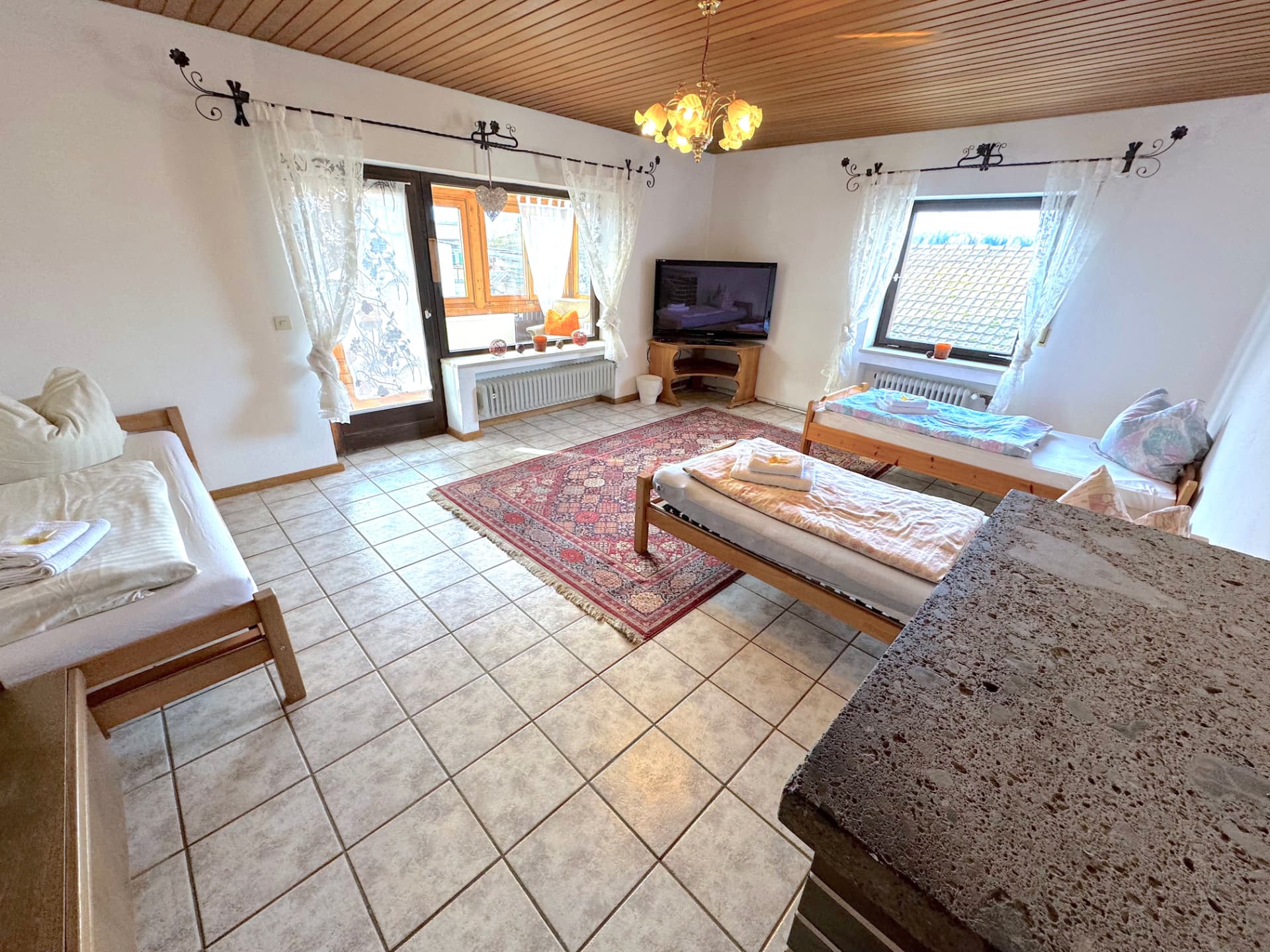 Helles Wohn- und Schlafzimmer mit drei Einzelbetten, Terrassentür, TV und Kronleuchter in Griesbach