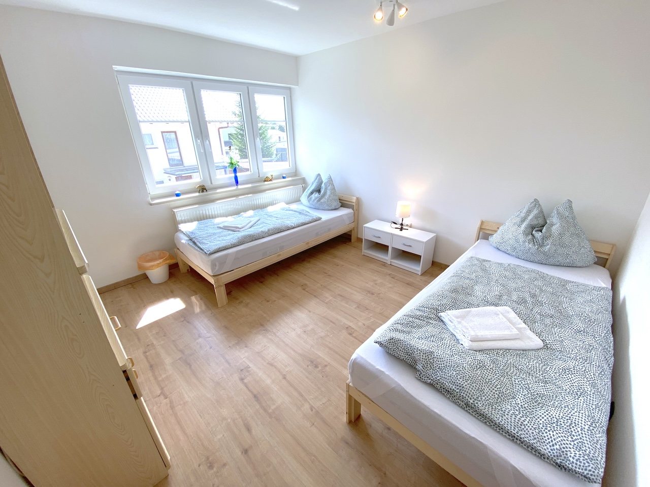 Zwei Einzelbetten auf hellem Laminatboden mit Fenster und grauen Vorhängen – Apartment in Kronwieden