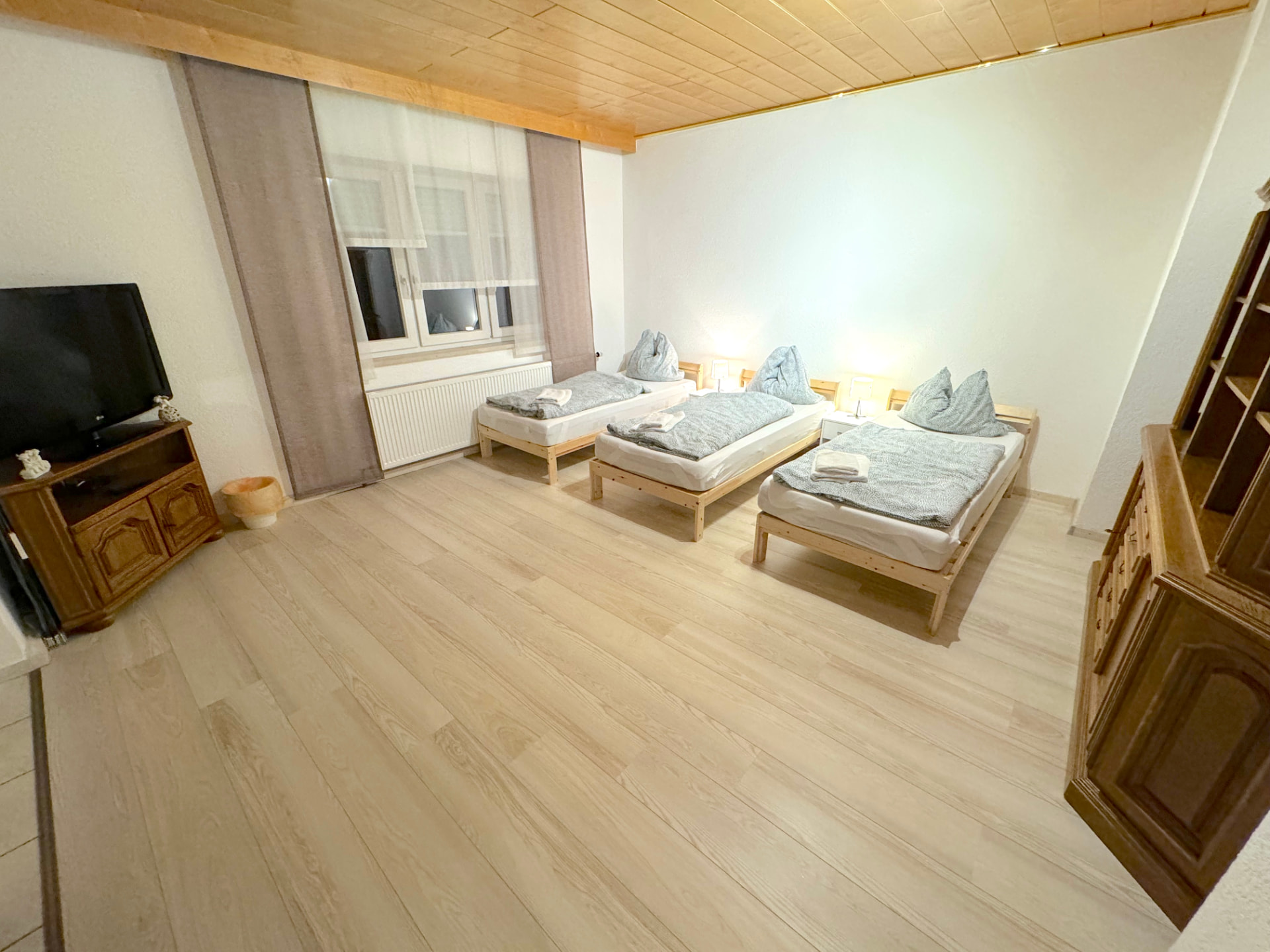 Apartment II in Kronwieden – Großer Schlafraum mit drei Einzelbetten, TV und Holzdecke