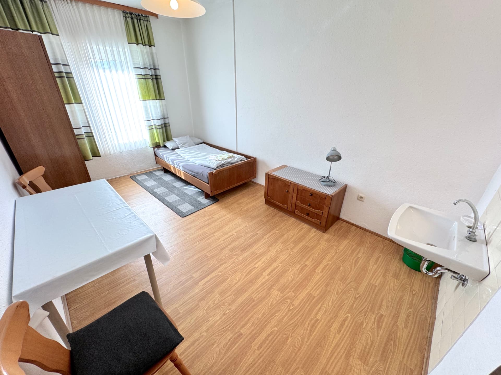 Einzelzimmer mit Bett, Tisch, Kommode und Waschbecken in Apartment III Mettenhausen