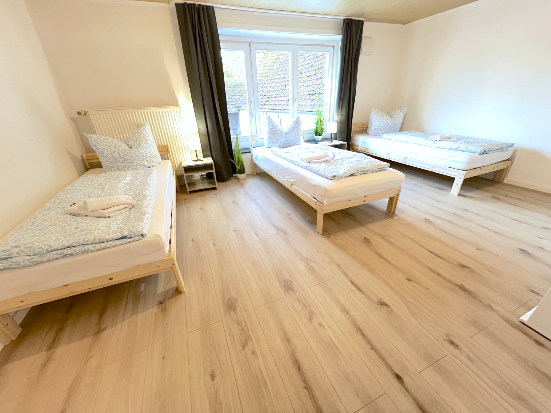 Helles Drei-Bett-Zimmer mit Holzbetten, Nachttisch und Fenster in Apartment III Großköllnbach