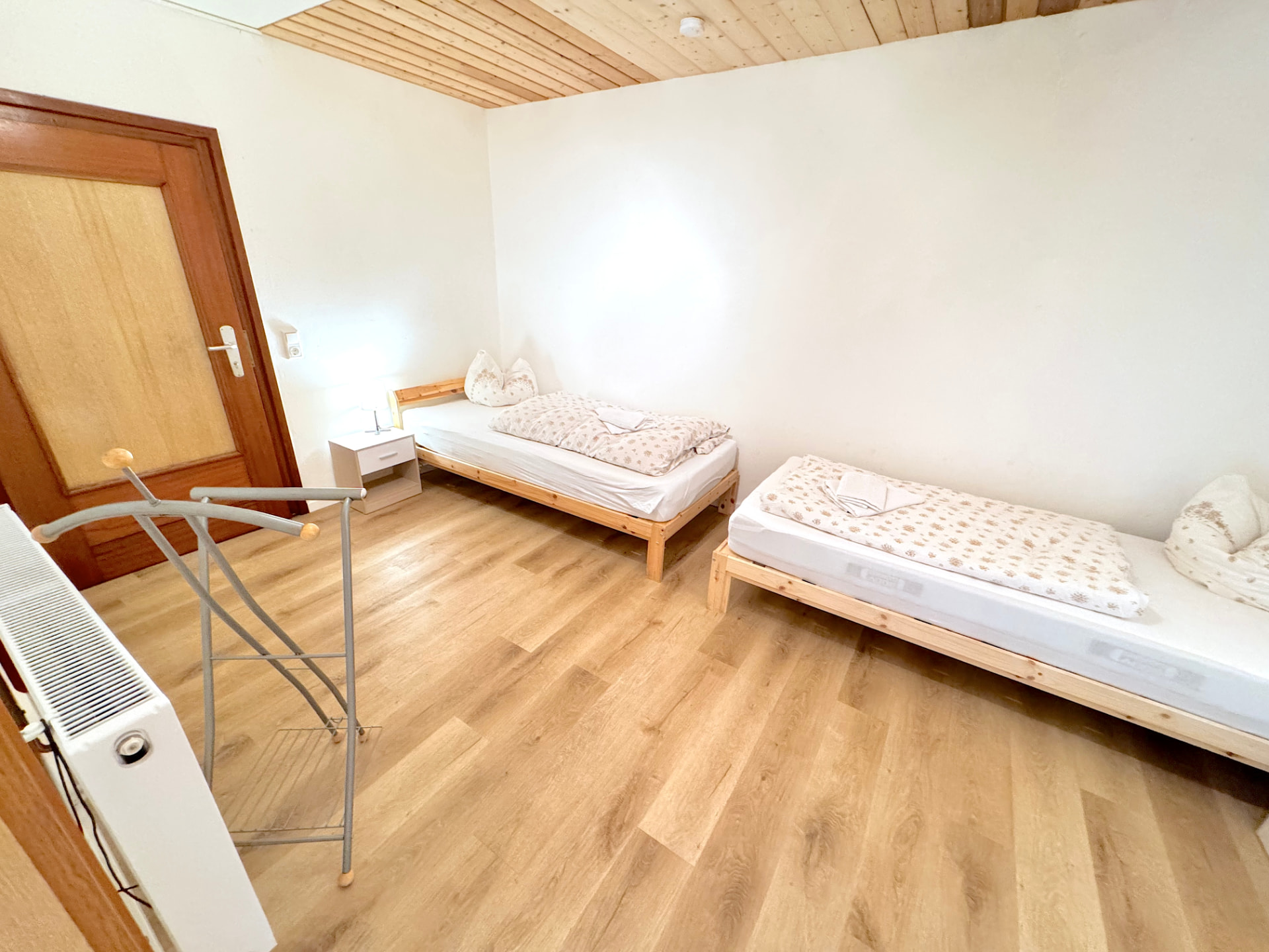Schlafzimmer mit zwei Einzelbetten, Holzdecke, Nachttisch und Kleiderständer in Apartment I Griesbach