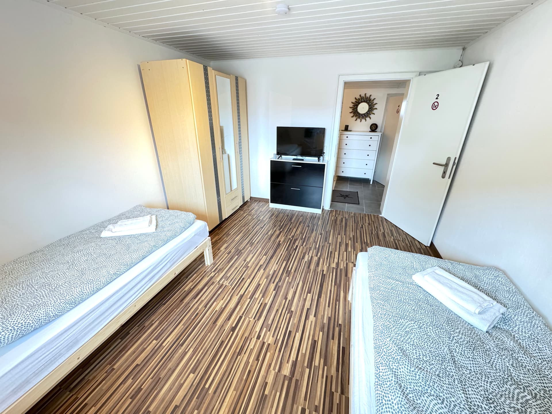 Apartmenthaus in Frontenhausen – Zimmer mit zwei Betten, Kleiderschrank, TV und Blick zum Flur