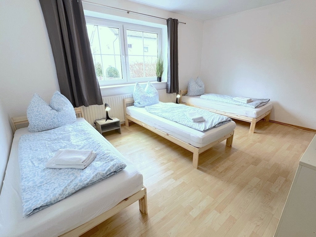 Drei Einzelbetten in L-Form mit Fenster und hellem Holzboden – Apartment in Dingolfing