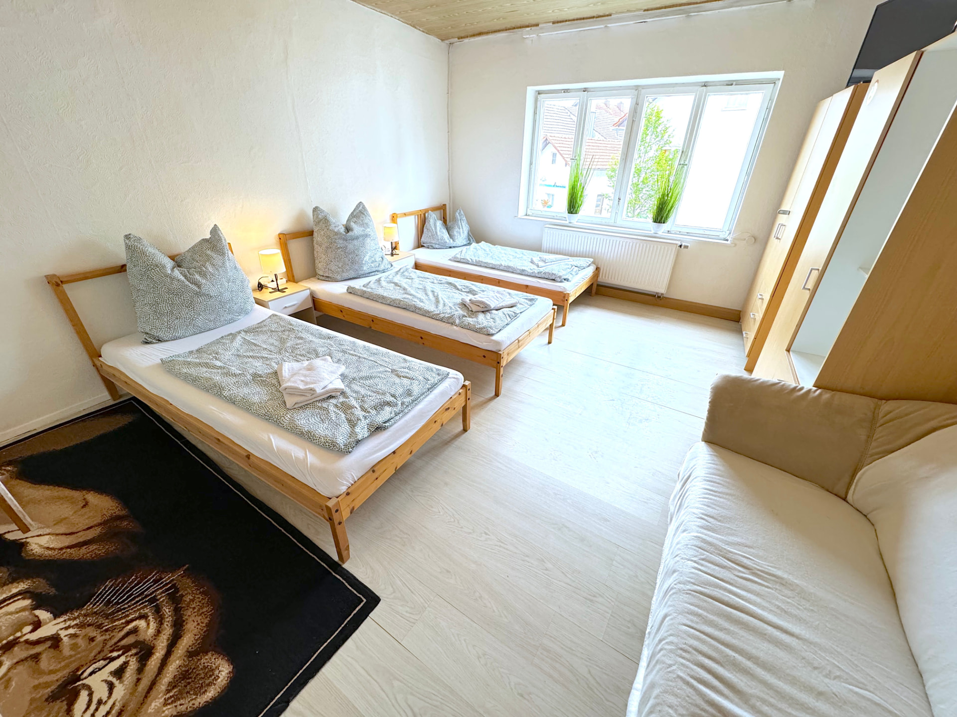 Großes Zimmer mit drei Einzelbetten, Sofa und Kleiderschrank im Apartmenthaus Großköllnbach