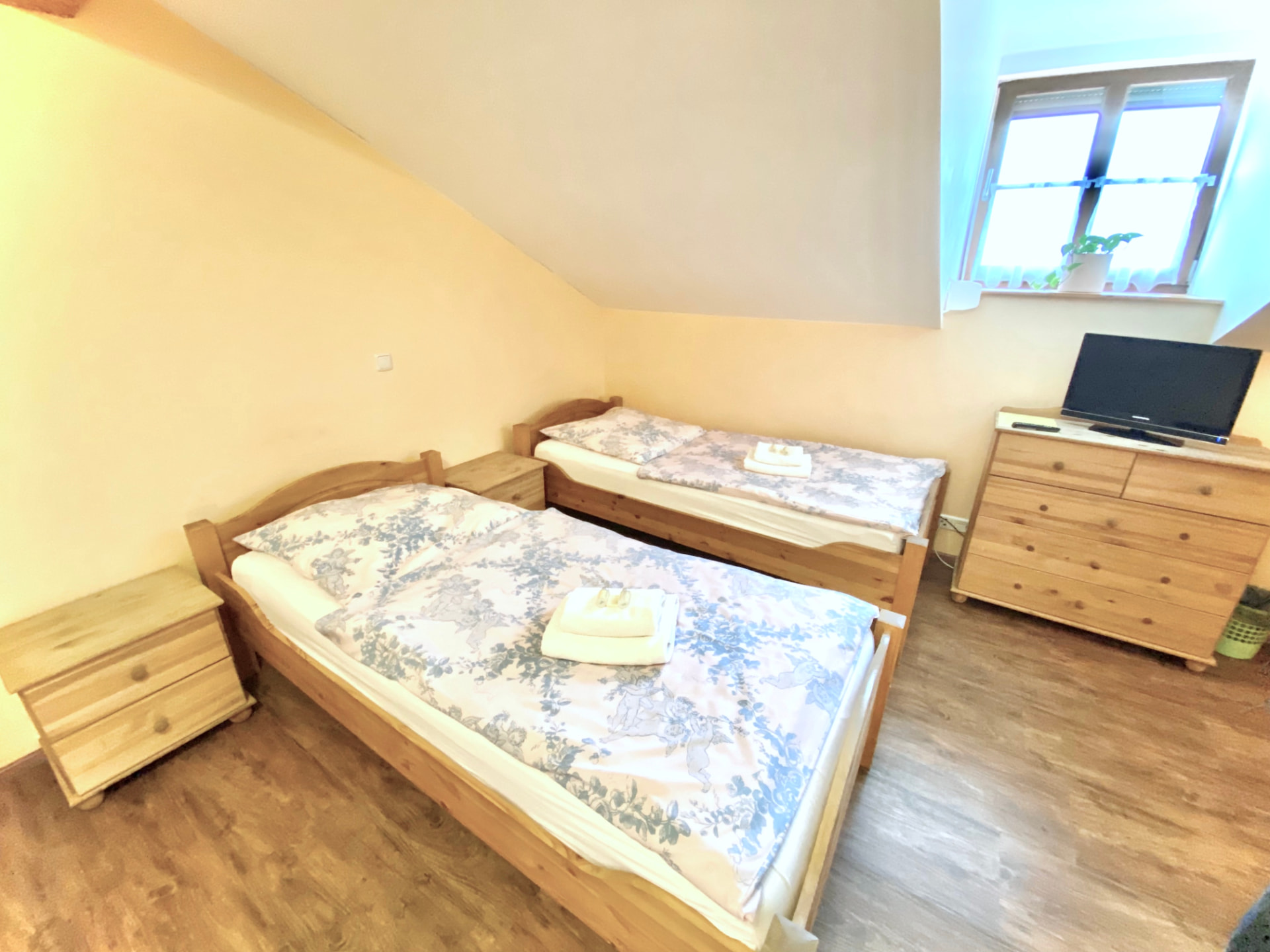 Zwei-Bett-Zimmer mit Holzbetten, Nachttischen und TV in der Pension Laurent Ranch Gottfrieding