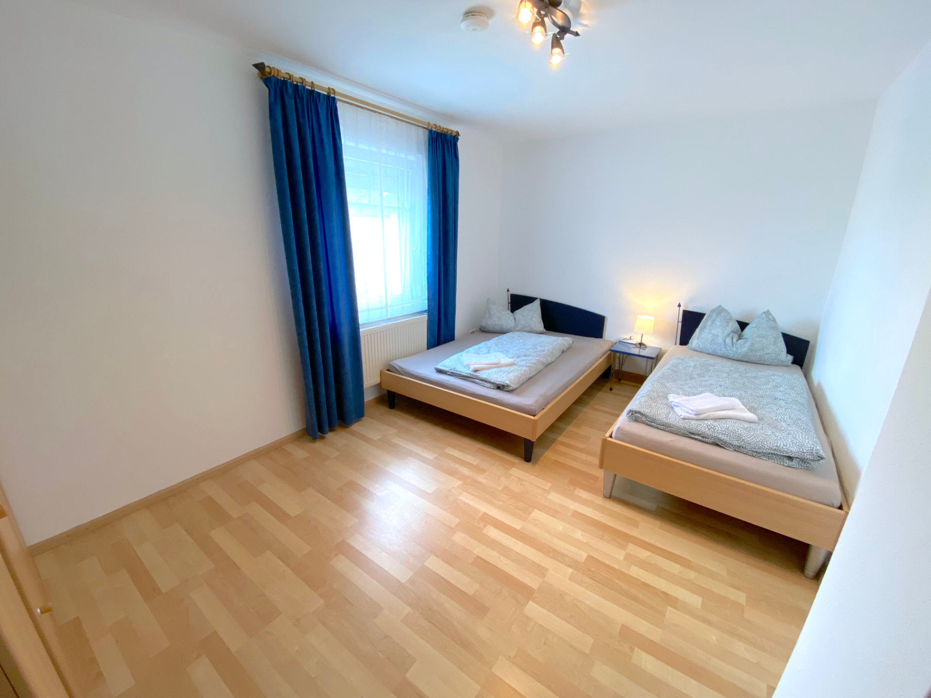 Apartment III in Kronwieden – Helles Schlafzimmer mit zwei Betten und blauen Vorhängen