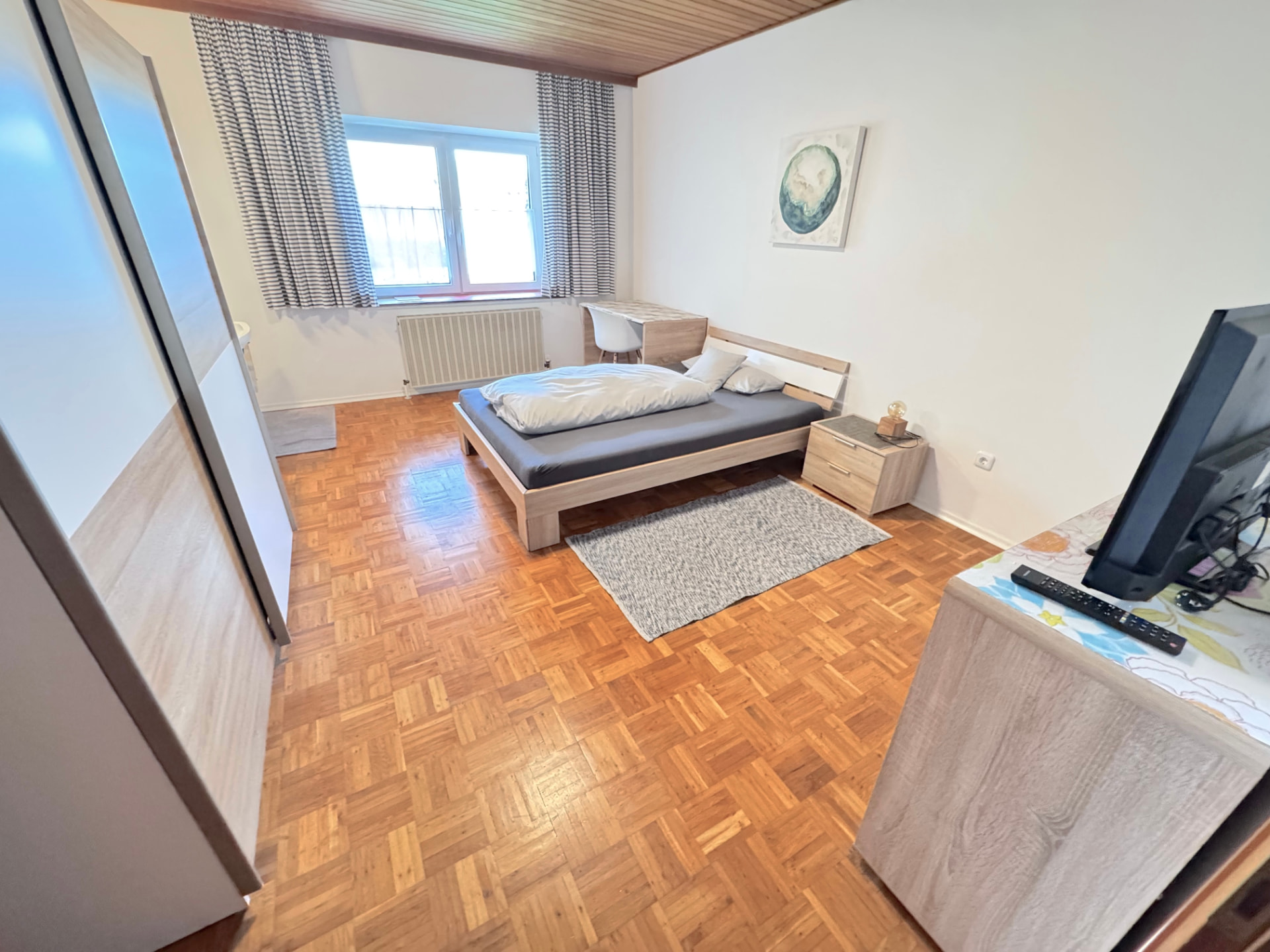 Helles Zimmer mit Doppelbett, Schreibtisch, TV und Parkettboden in Apartment III Mettenhausen