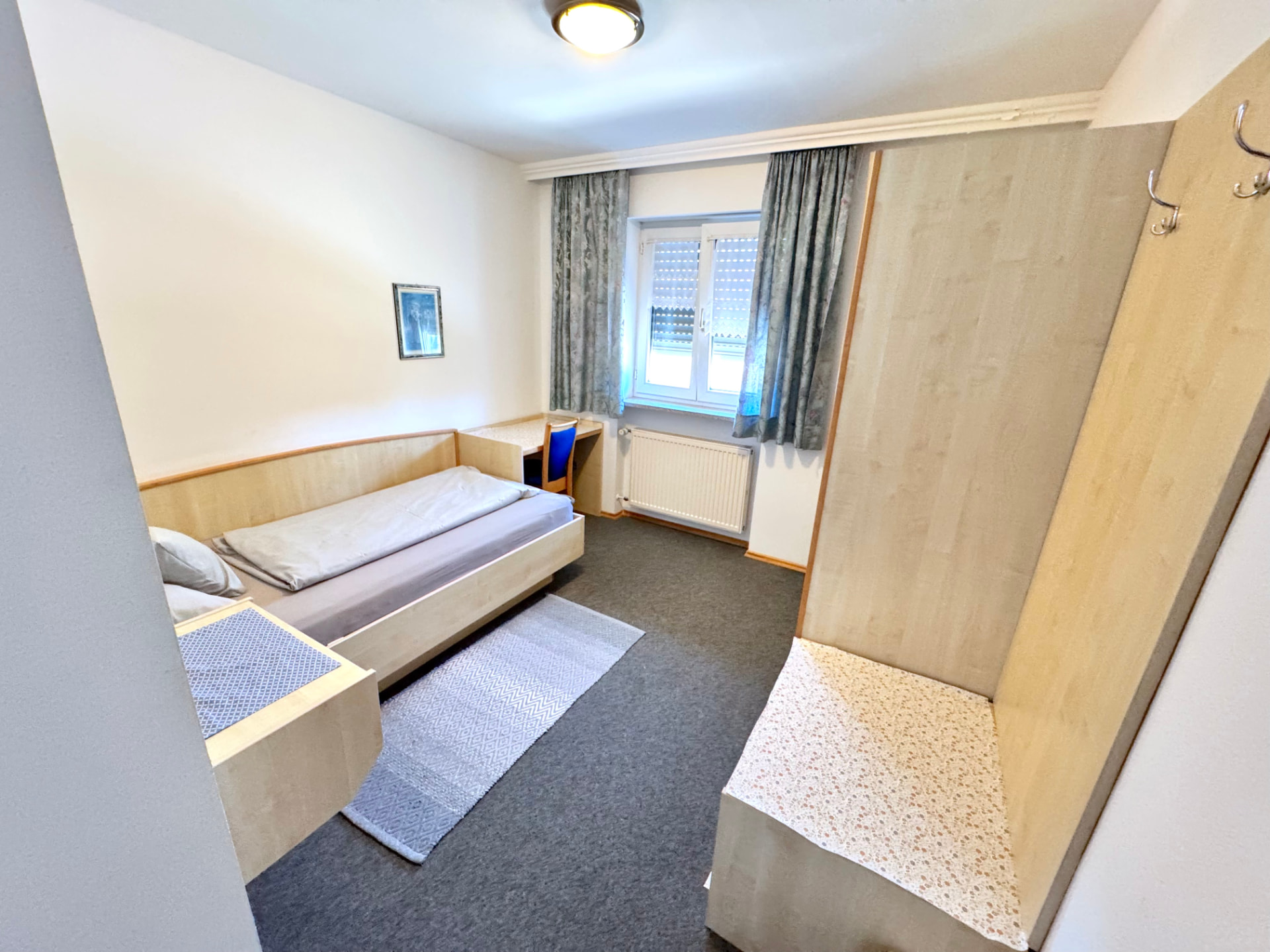 Einzelzimmer mit Bett, Schreibtisch, Garderobe und Teppich in Mettenhausen