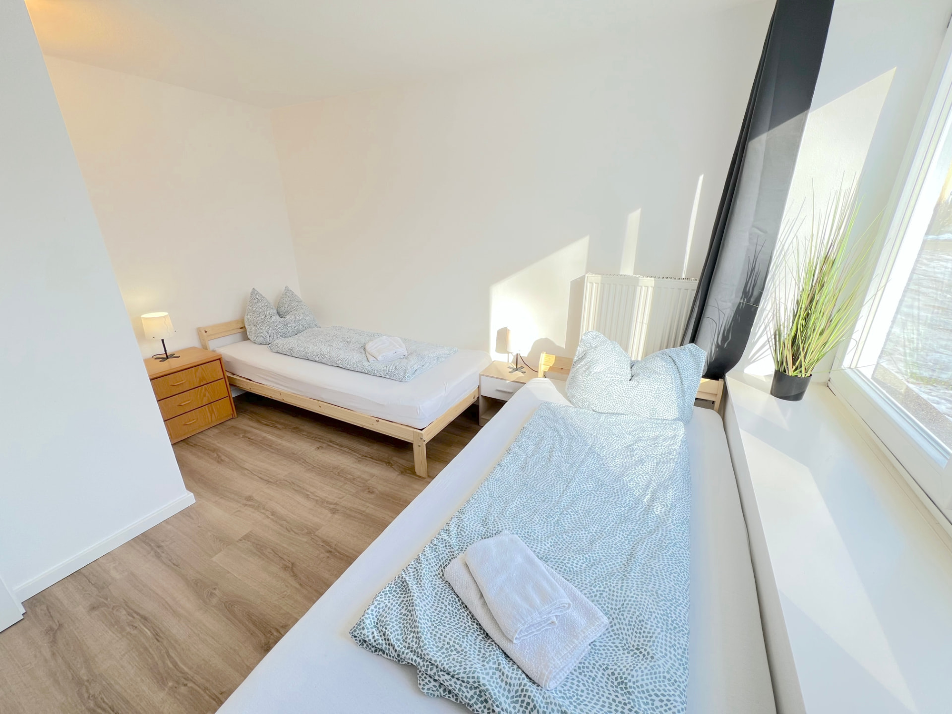 Helles Zwei-Bett-Zimmer mit Holzbetten, Nachttischlampen und großem Fenster in Apartment II Großköllnbach